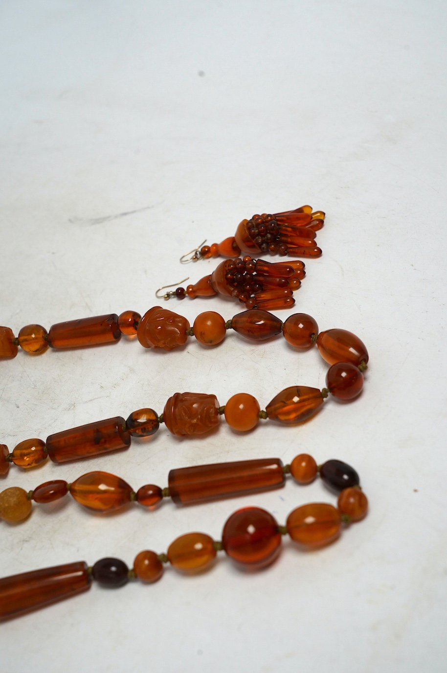 Two amber bead necklaces including Chinese with carved busts, 76cm and a pair of drop earrings, gross weight 145 grams. Condition - poor to fair